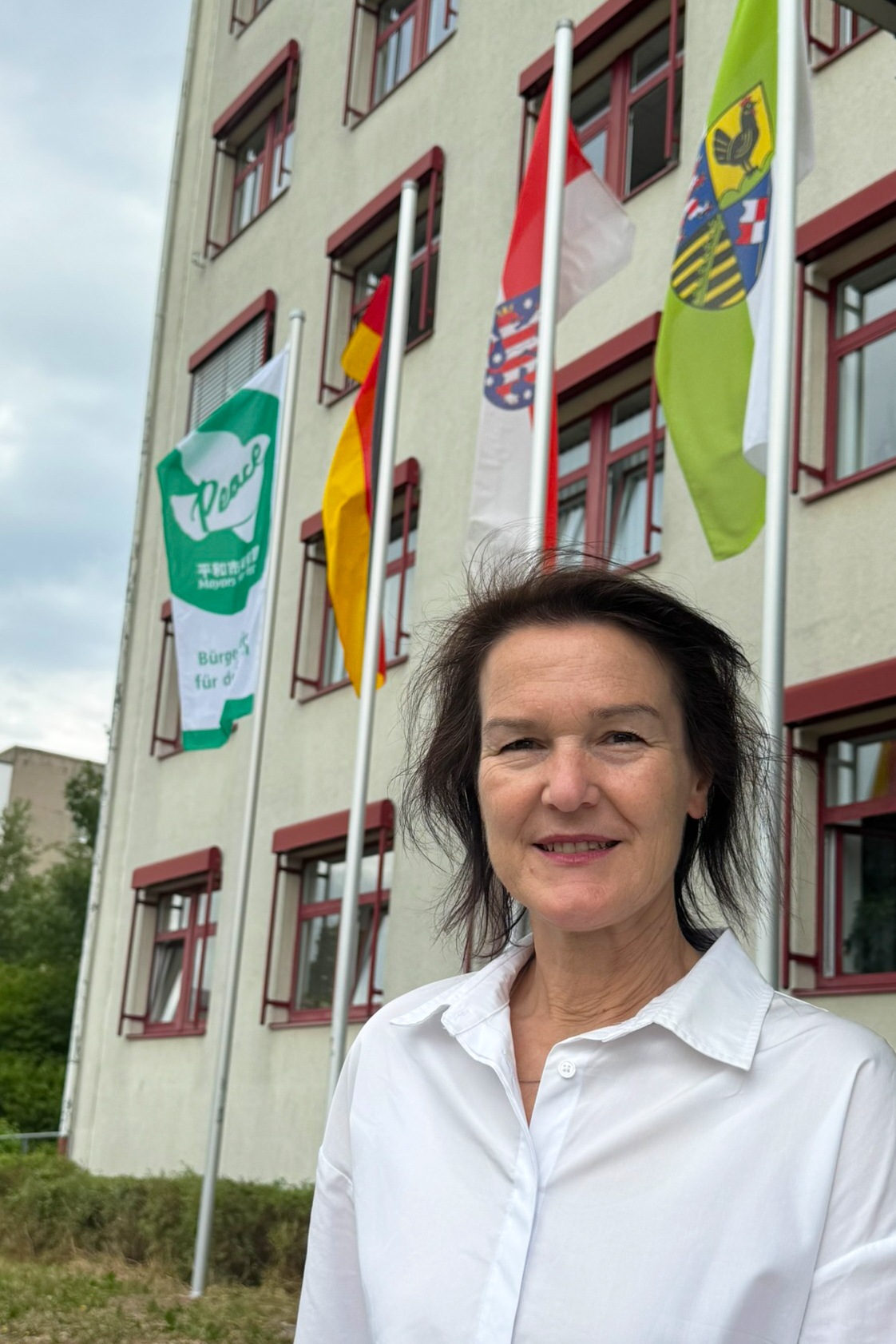 Landrätin Peggy Greiser steht vor der gehissten Mayors-for-Peace-Flagge am weltweiten Flaggentag am 8. Juli vor dem Meininger Landratsamt.