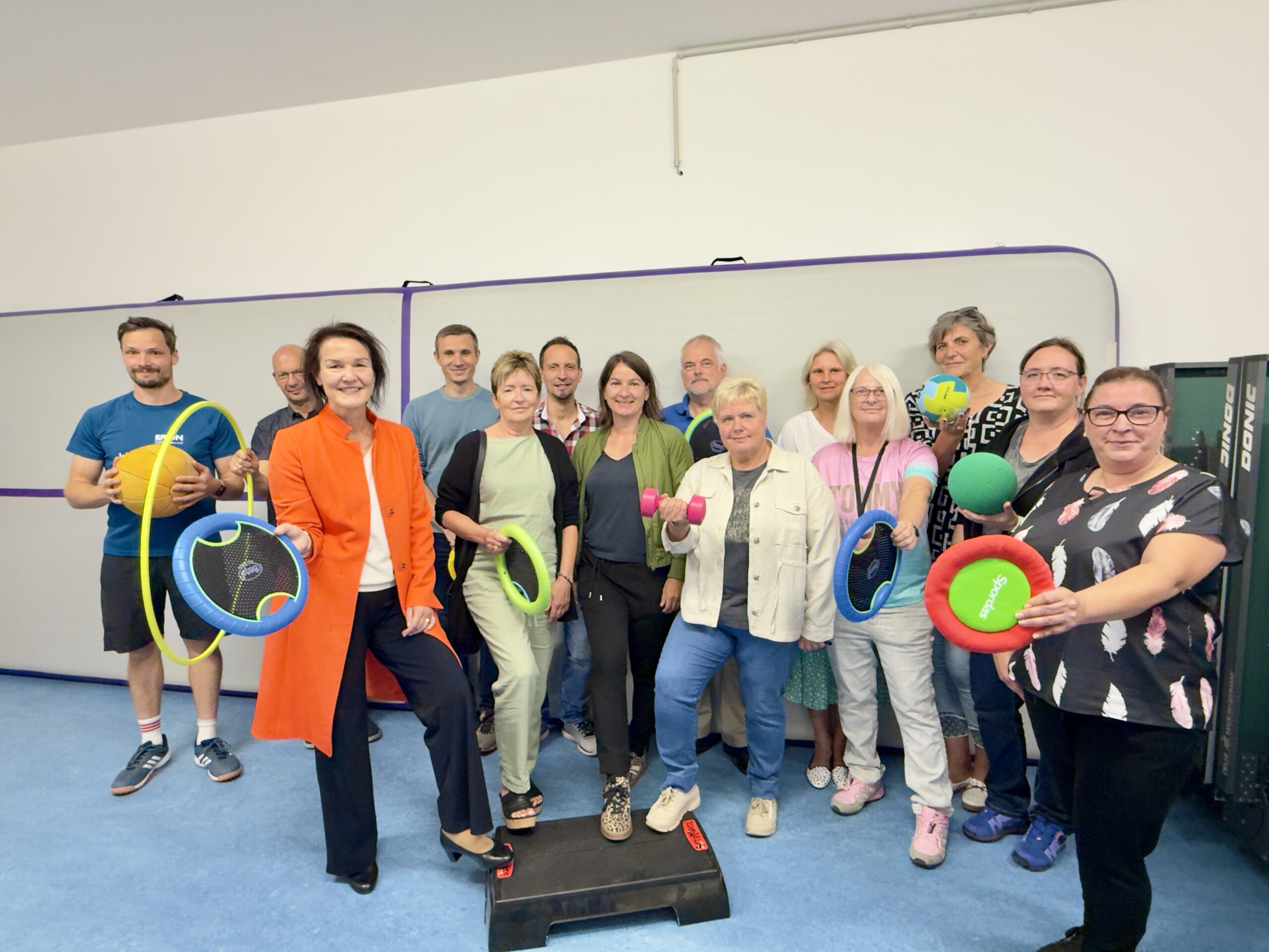 Landrätin Peggy Greiser präsentiert mit Martin Schuster und Sandra Schilling vom Fachdienst Bau und Gebäudeverwaltung, Schulleiterin Manuela Klaedtke, Sportlehrer Sigmar Holland-Moritz und weiteren Lehrern den neuen Lagerraum der Regelschule Wasungen.